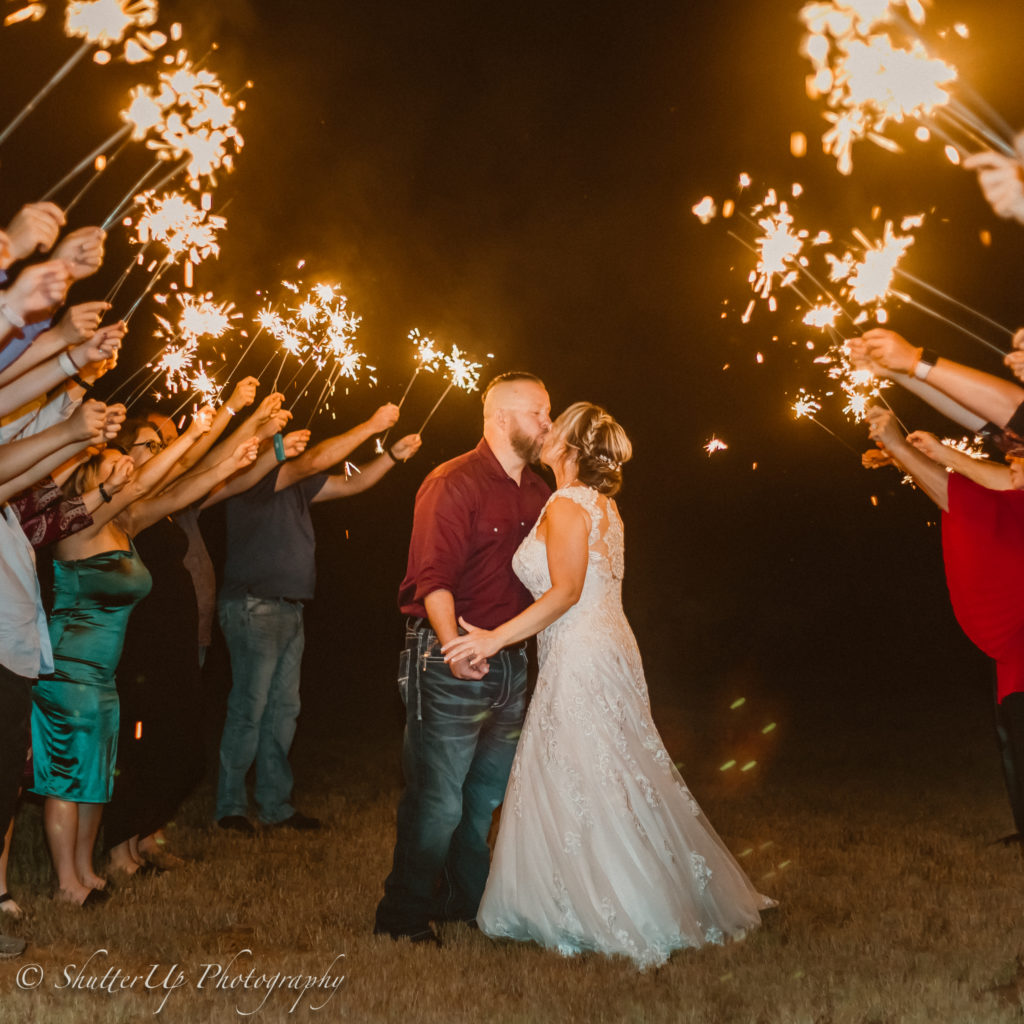 Newlyweds joyfully Kisss and exit  their wedding reception surrounded by a sparkling send-off 