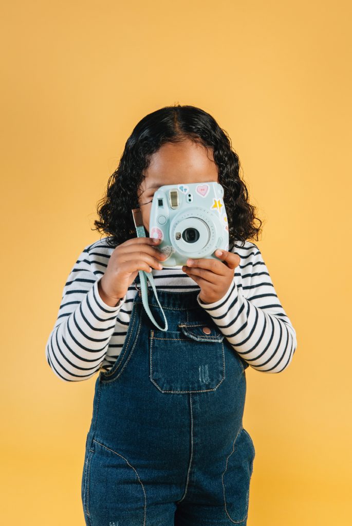 toddler girl holding a polaroid camera up to her face. to Keep Children Entertained at Your Wedding